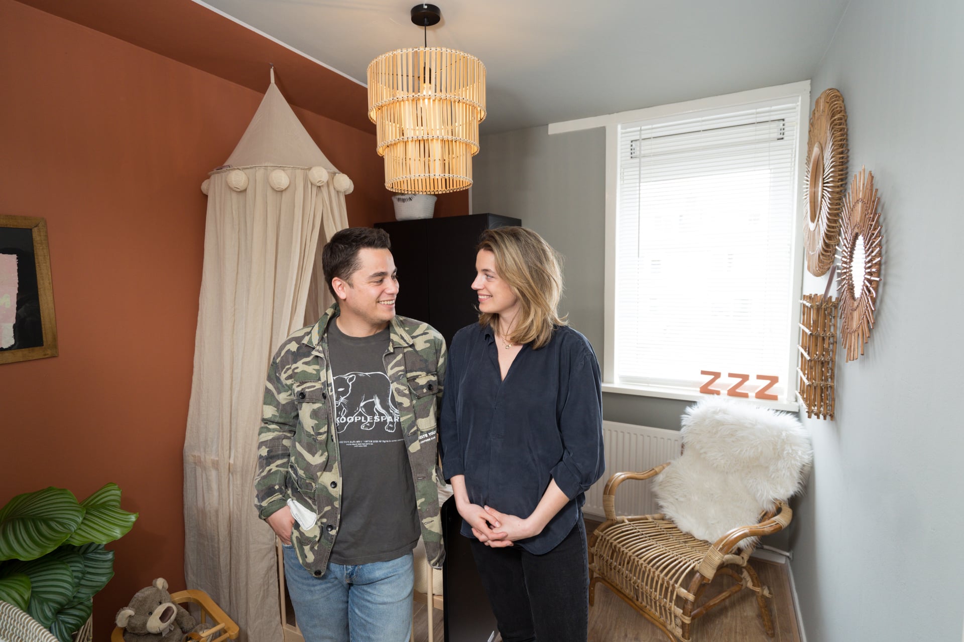 Twee personen staand in een gezellige kamer met stoel en hanglamp