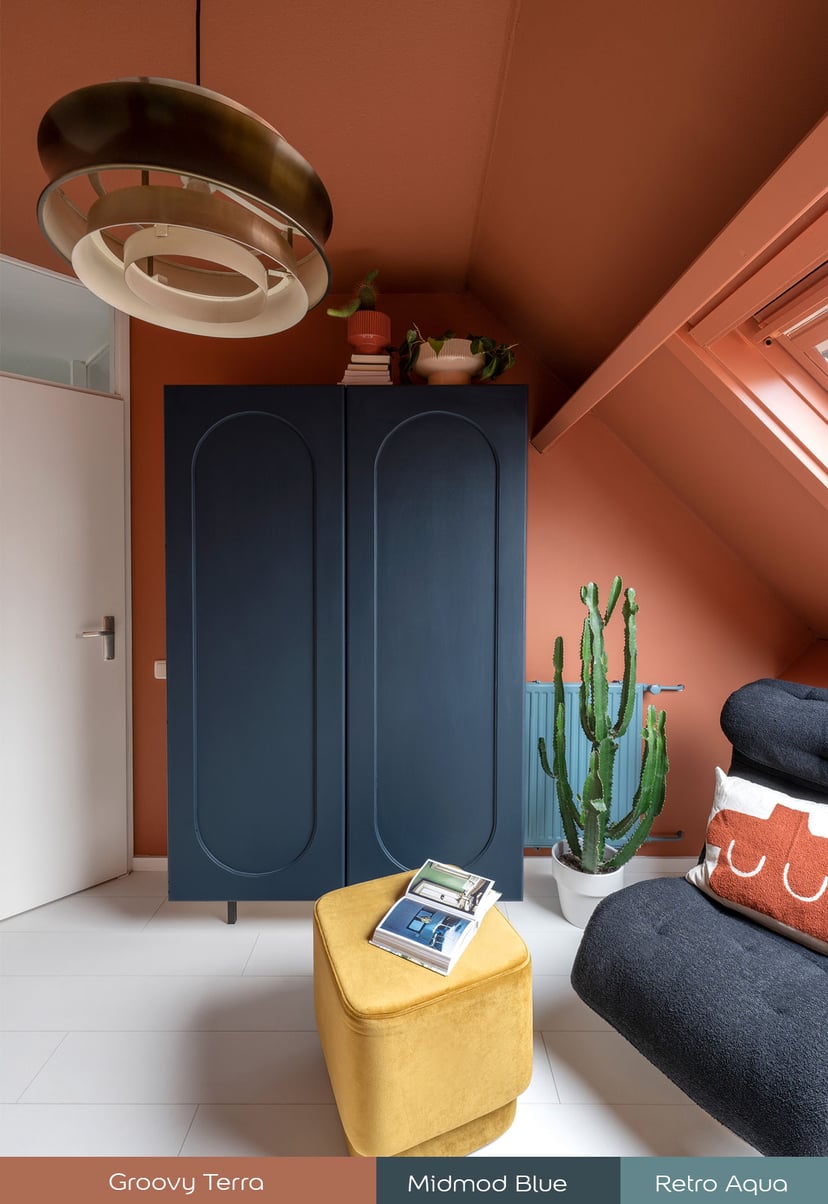 Slaapkamerhoek met donkerblauwe kast, terracotta muren, gele poef en een grote cactus