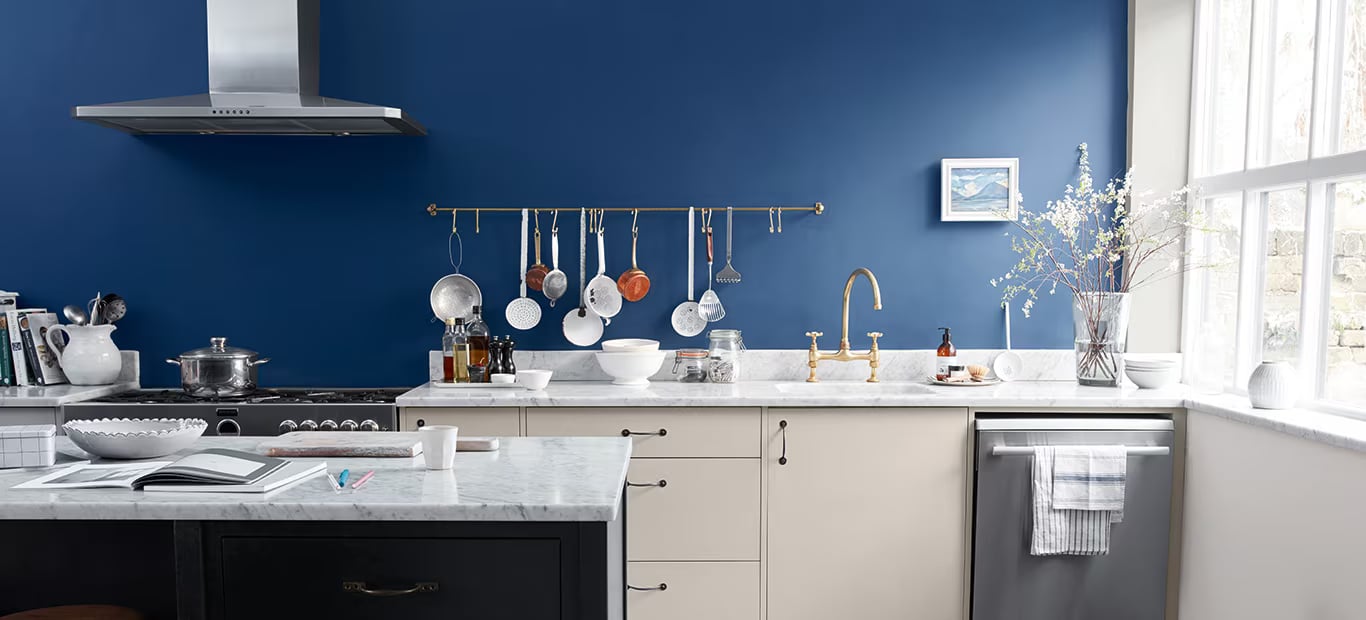 Moderne keuken met een blauwe accentmuur, witte werkbladen en hangend kookgerei
