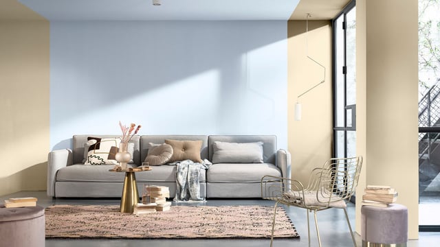 Licht modern woonkamer met een lichte bank, een vloerkleed met patroon, salontafel en grote ramen.