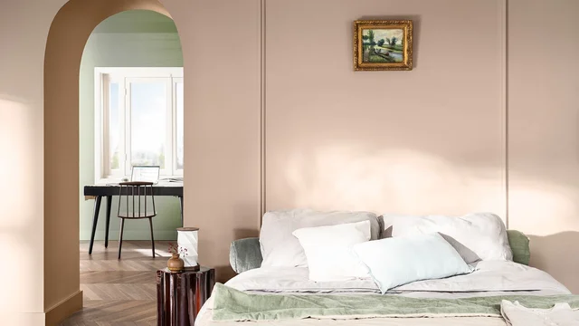 Slaapkamer met groot bed, groene plaid en ingelijst schilderij, met zicht door een boog naar een bureau