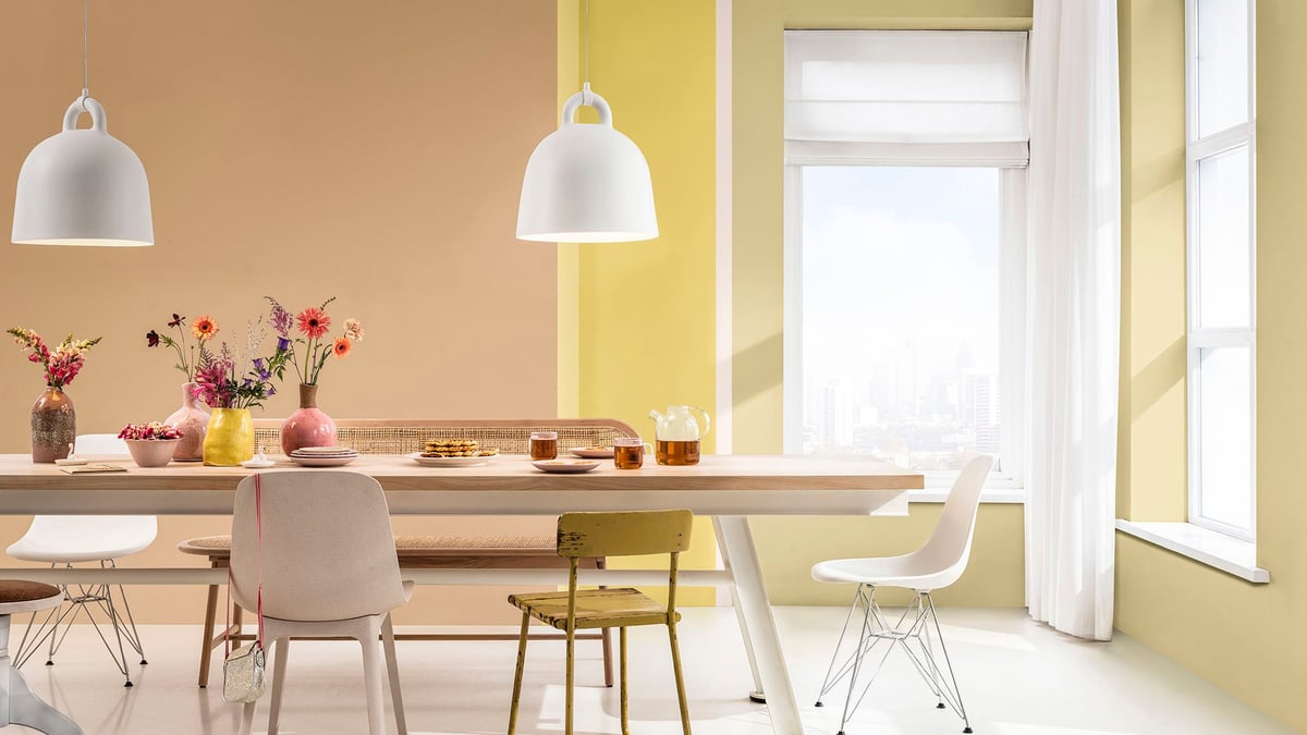 Lichte eetkamer met pastelgekleurde muren, een houten tafel en witte hanglampen.