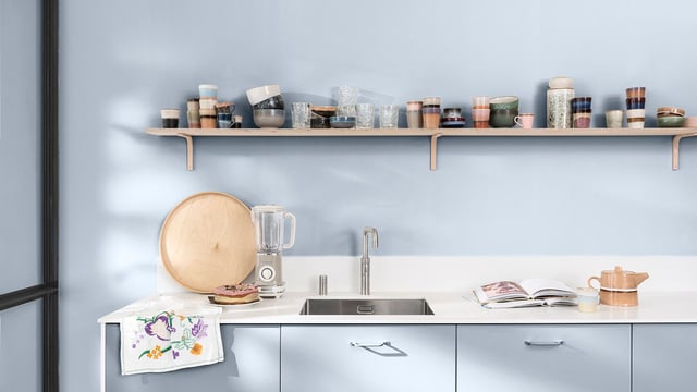 Lichtblauwe keuken met wit werkblad, spoelbak, waterkoker en kopjes op open planken