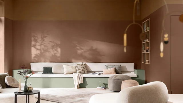 Moderne woonkamer met beige bank, sierkussens, salontafel met bloemen en natuurlijk licht.