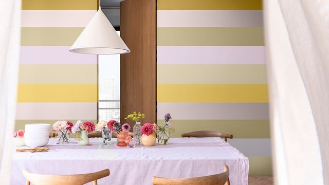 Eettafel met bloemen in vazen, wit-gele gestreepte muur en hanglamp in de keuken