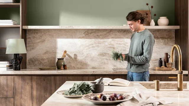 Man staat in een moderne keuken en houdt een bosje kruiden bij het aanrecht