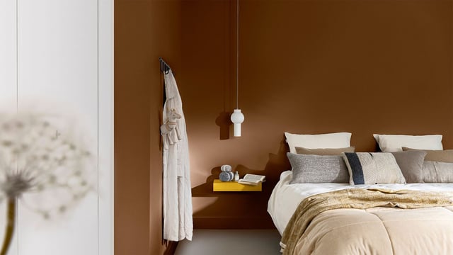 Warme, moderne slaapkamer met netjes opgemaakt bed, kussens, wandplanken en hanglamp.
