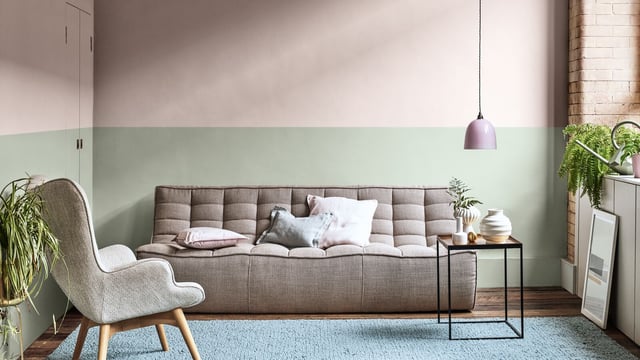 Moderne woonkamer met grijze bank, blauw kleed, lichtgroene en grijze muur, bijzettafel, lamp en planten