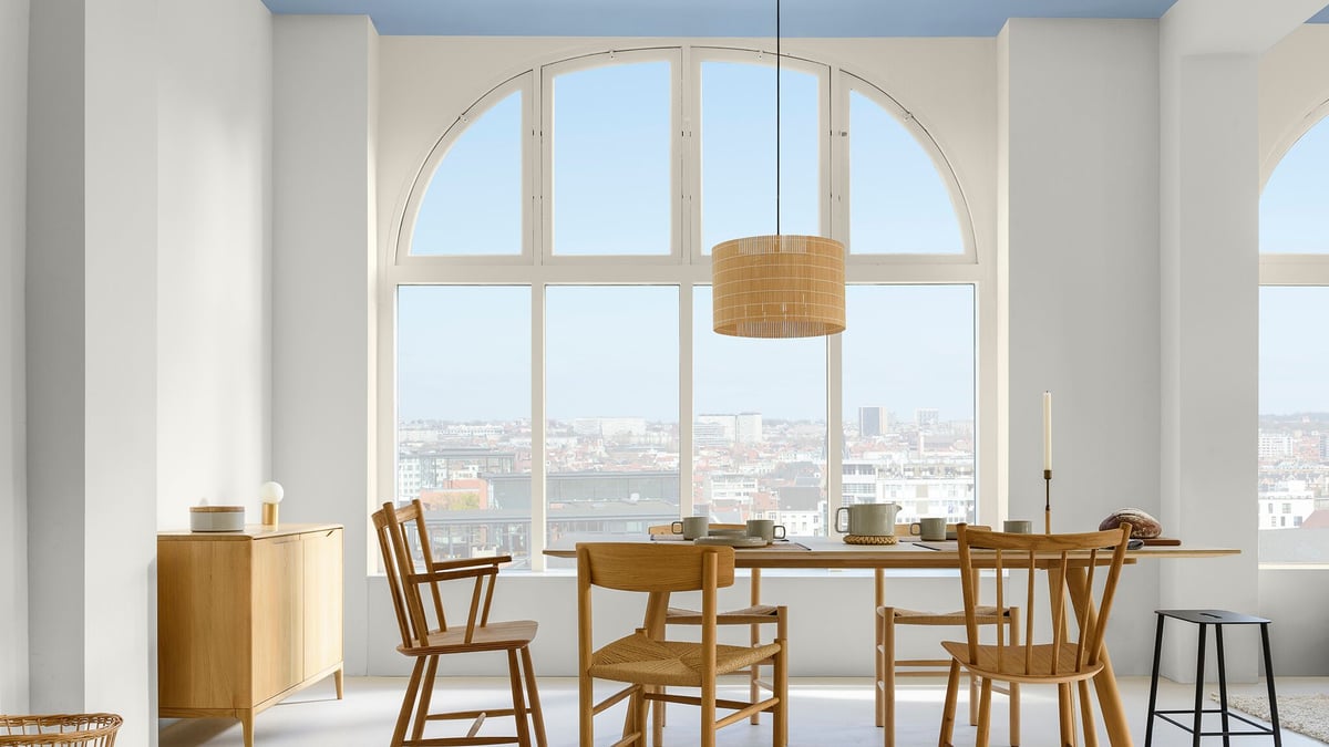 Lichte eetkamer met houten tafel en stoelen onder een hanglamp, bij een groot boograam met uitzicht op de stad
