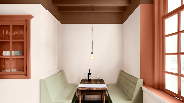 Gezellige hoek met houten tafel, banken en hanglamp, naast grote raampartij en witte muren