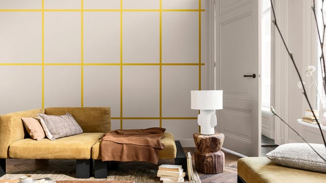 Helder woonkamer met mosterdgele bank, kussens en een witte vloerlamp.