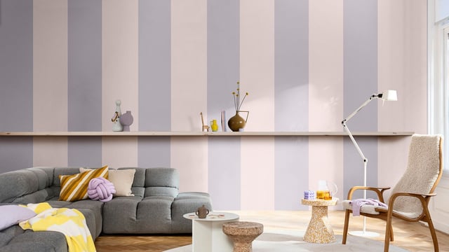 Lichte woonkamer met grijze bank, gele kussens en een fauteuil bij het raam.