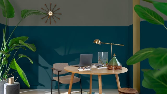 Thuiswerkplek: ronde houten tafel met laptop, lamp en planten tegen een blauwe muur