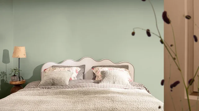 Sfeervolle slaapkamer met tweepersoonsbed, lampje en zachte groene muur