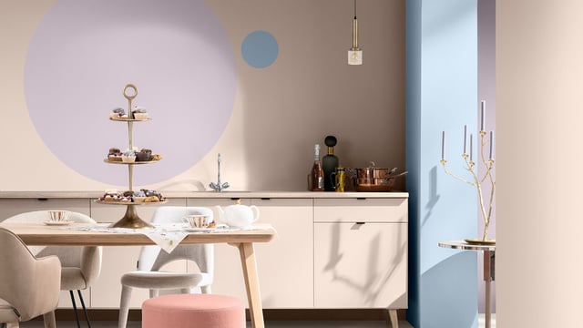 Lichte keuken met witte keukenkasten, houten tafel, roze stoel en pastelkleurige muren met decoratie