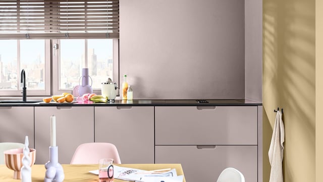 Moderne keuken met lichte kasten, werkblad met spullen en uitzicht op de stad via een groot raam.