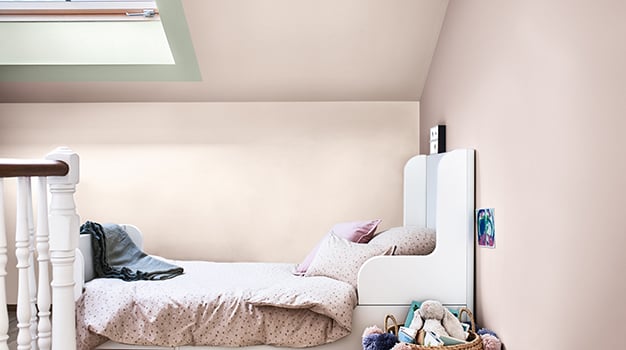 Kinderbed onder een schuin plafond met beige muren, een dakraam en een mand met knuffels