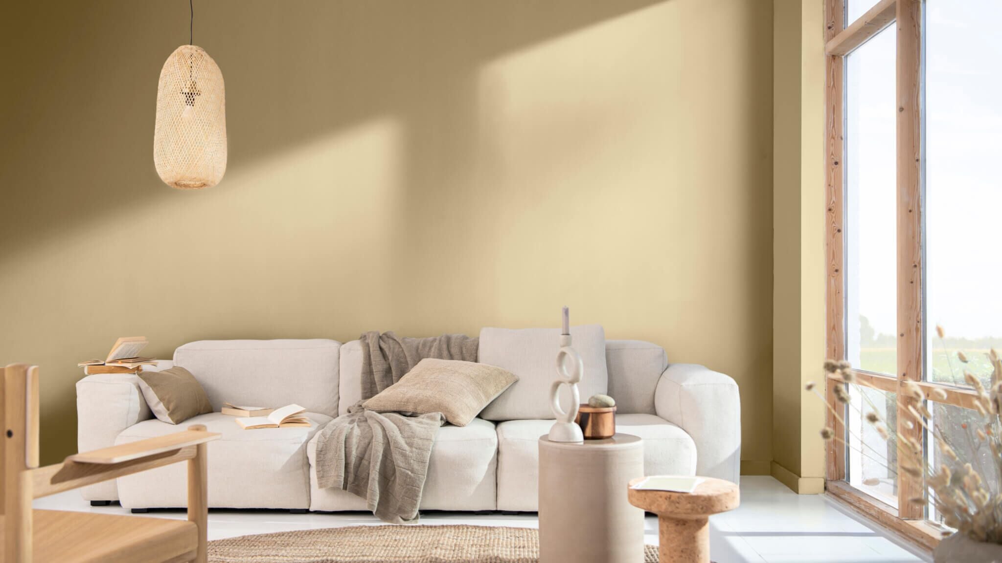 Gezellige woonkamer met een lichte bank en warme beige muren naast grote ramen.